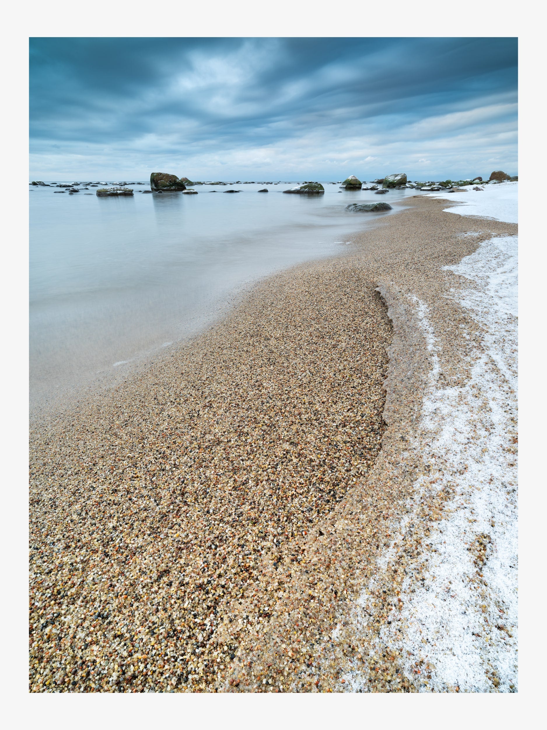 Rocks in the Sea and Sandy Shore under a Cloudy Sky