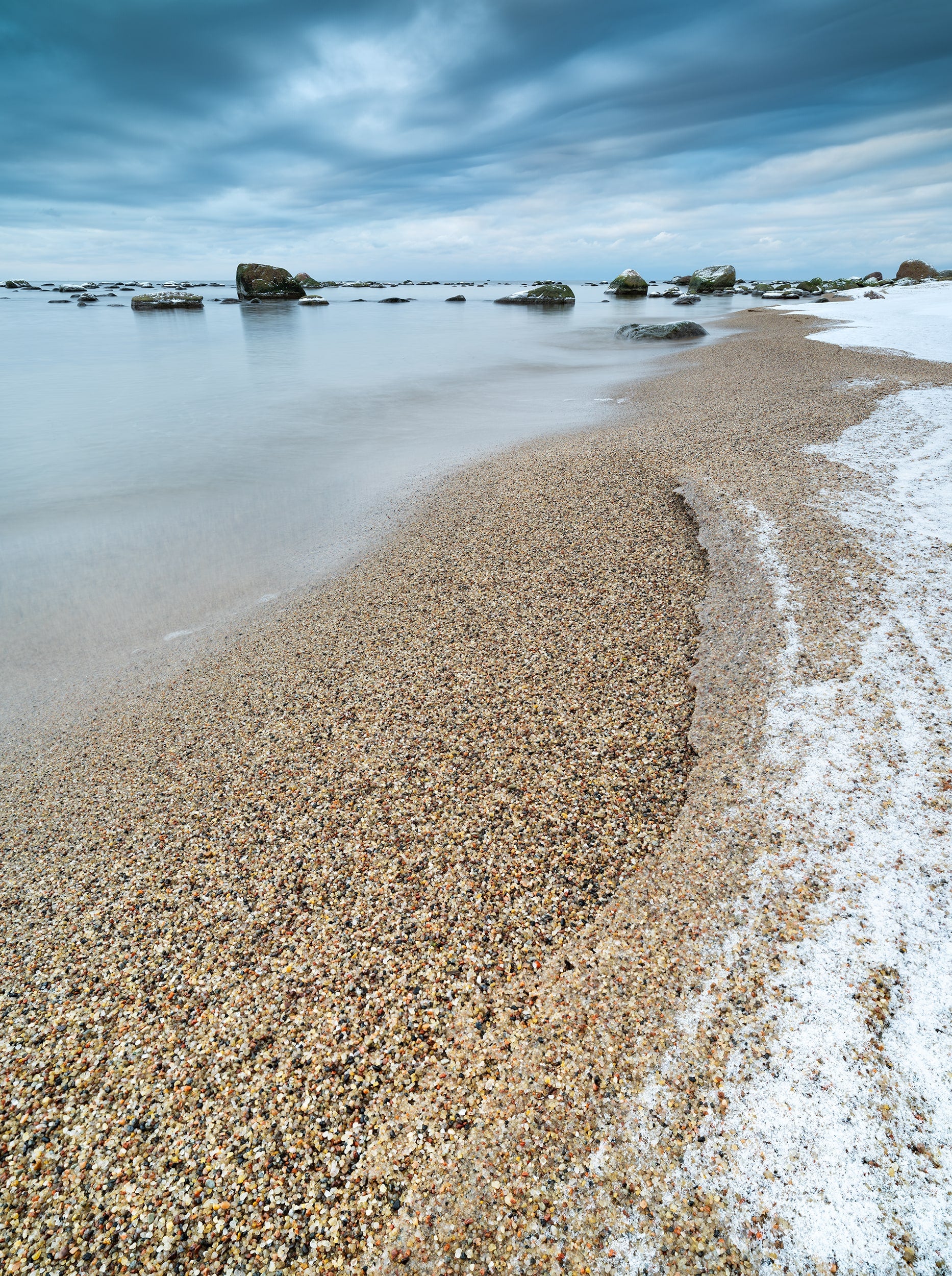 Rocks in the Sea and Sandy Shore under a Cloudy Sky
